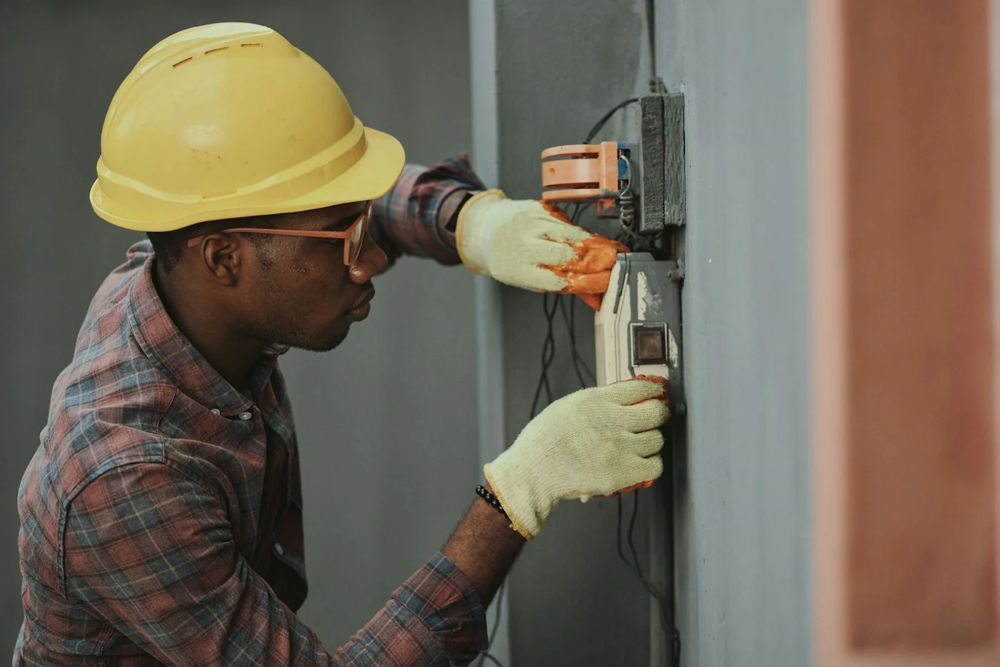 Technician installing electrical equipment with protective gloves and a hardhat